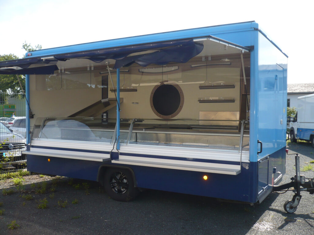 Verkaufsanhänger mit leichten Gebrauchsspuren für den Betrieb auf Wochenmärkten oder festen Standplätzen. Schrägauslage an der Heckseite, Lampenblende mit Sichfeldern und Facettenscheiben in Verkaufsöffnung.