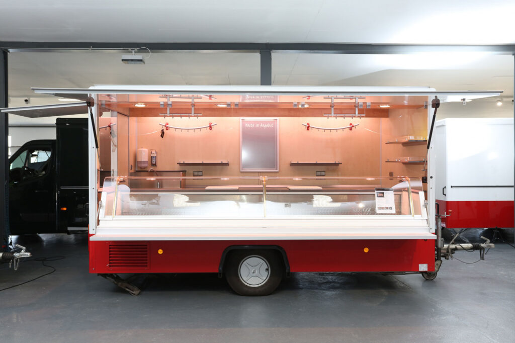 Sehr gepflegter Anhänger mit herausfahrbarer Panorama-Kühltheke 670 mm tief, Bäro-BFL-Stahler über Theke.  1/2 Schaufenster in der Heckseite über der Theke mit Vordachklappe. Anhänger ist außen nur 2.150 mm breit.