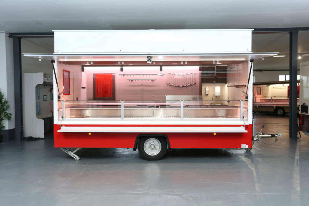 Sehr junger und gepflegter Verkaufsanhänger mit senkrechter Panorama-Thekenverglasung. Kühltheke mit 740 mm Auslage und verstärkter Kühlleistung, zusätzliche Acrylglas-Abdeckung für die Theke, 3 Kühlfächer unter der Theke, Deckenklimagerät mit Fernbedienung, beheizter Körperschutzkante, LED-Bäro-Einbauleuchten, Edelstahl-Dosenregal, Werbefront 3-seitig am Dach montiert, 400 V-Steckdose, uvm.