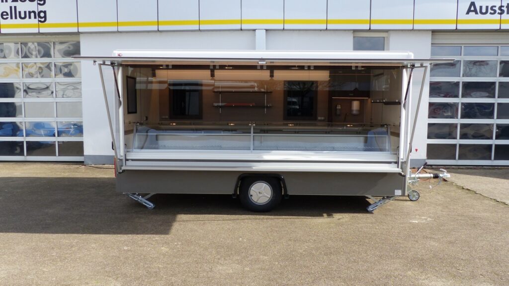 Hochwertiger Verkaufsanhänger CLEVERplus 3:-beheizte Körperschutzkante, verschiedenes Thekenzubehör (Aufnahmehaken für Tüten, Waagenplatte uvm.), BÄRO-LED-Strahler, Werbetafel mit Glasschriftfeld