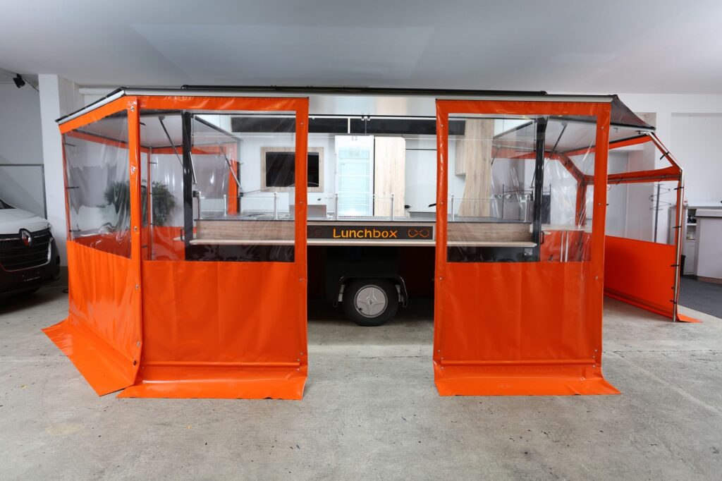 Hochwertiger Verkaufsanhänger:-drei Verkaufsseiten, diverse Imbissgeräte (1400 mm Bratgerät, 2-Korb Fritteuse, Bainmarie, etc.), zwei LIEBHERR Kühlschränke, einhängbarer Abfalleimer, LED-Lichtleiste HO, beschriftete und hinterleuchtete Thekensenkrechte, beschreibbare Lampenblende mit Glasschriftfeld, Werbetafel mit Glasschriftfeld -komplette Einplanung durch Trevira - in orange