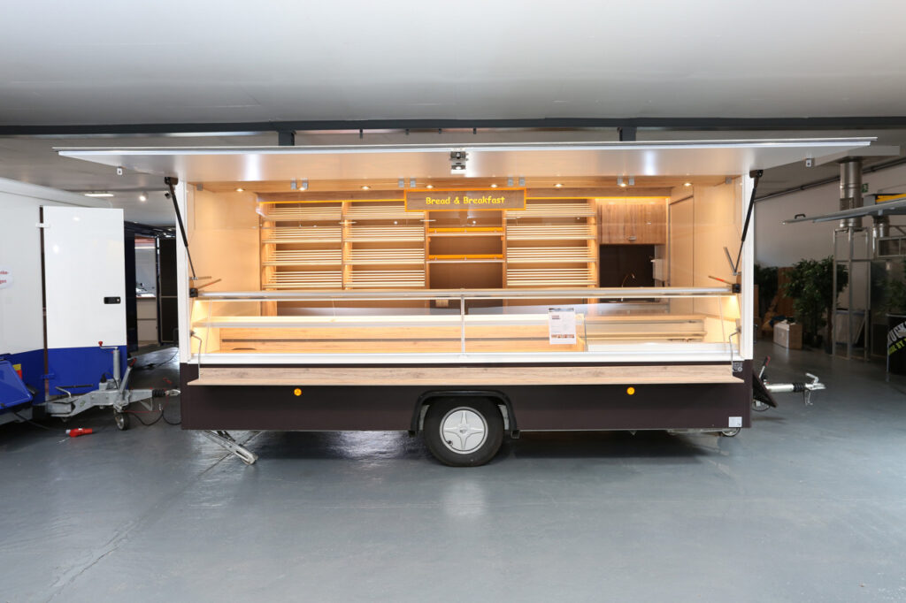 Gepflegter Verkaufsanhänger mit neuster LED-Lichttechnik und hoher Lichtleistung. Die Brotborde haben Aluminium-Rundstäbe und gehen über 4  Etagen an der Rückwand, ebenso befindet sich dort ein Handelswarenbord und Platz für eine Kaffeemaschine. Unter der hinteren Arbeitsfläche ist Platz für 5 Nachschub - Kuchenbleche.