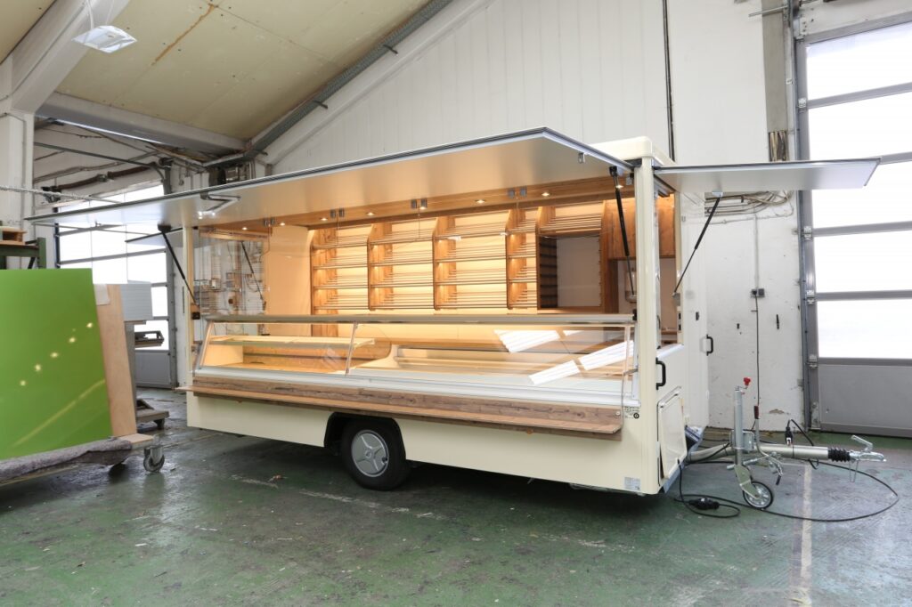 Backwaren Verkaufsanhänger mit einer Verkaufstheke von 4,5m, die Trockentheke misst 2m und der Kühlbereich beträgt 2,5m. Die Kühltheke hat eine stille Kühlung. An der Verkaufsrückwand befinden sich Brotborde und ein Nachschubregal. Unterhalb der Brotborde befindet sich das Hygienepaket.