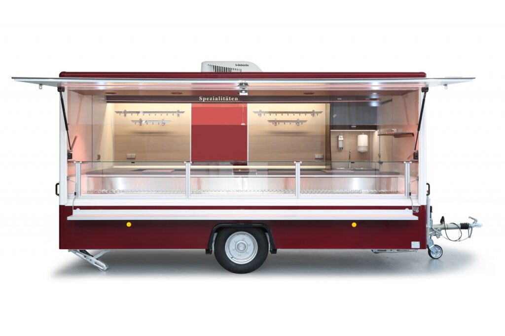 Verkaufsanhänger mit einer Verkaufskühltheke von 4,5m. Verbaut ist ein Stilles Kühlsystem. Die Arbeitsfläche an der Verkaufstheke ist mit einer beheizten Körperschutzkante ausgestattet. An der Verkaufsrückwand befinden sich 2 Hakenschienen aus Edelstahl und eine Werbetafel  mit Glasschriftfeld. Unterhalb der Hakenschienen befinden sich Unterschränke und das Hygienepaket.