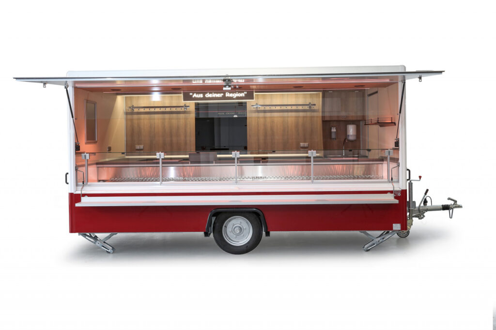 moderner Verkaufsanhänger-Kühltheke mit 740 mm Thekenauslage und Doppelkühlfach für 4 E-Kisten-Hakenschienen, Schalttafel 400 Volt, Glaswerbetafel, senkrechter Thekenaufsatz und Körperschutzkante mit integrierter Heizung