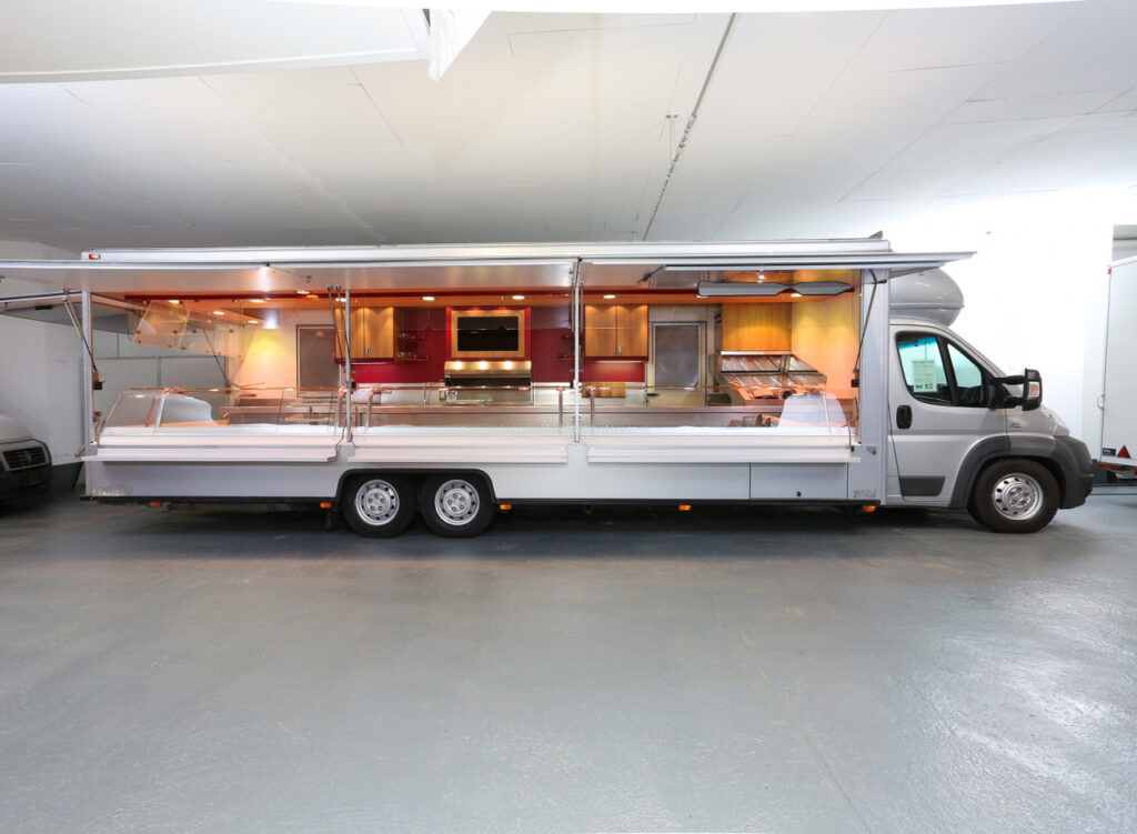 Fischverkaufsmobil mit 9,50m Kühltheke mit Leistungssteigerung, 3 Kühlfächern und 2 Kühlschränke von außen bestückbar.-Ausstattungsdetails: Gekühlte Schrägaslage, Ubert Imbissanlage mit Griddlebräter BGG 60, Friteuse KF 4 und integrierter Abzugshaube, Wiesheu Backofen Minimat, LCD-Rückfahrvideosystem, Unterflur Abwassertanks uvm.