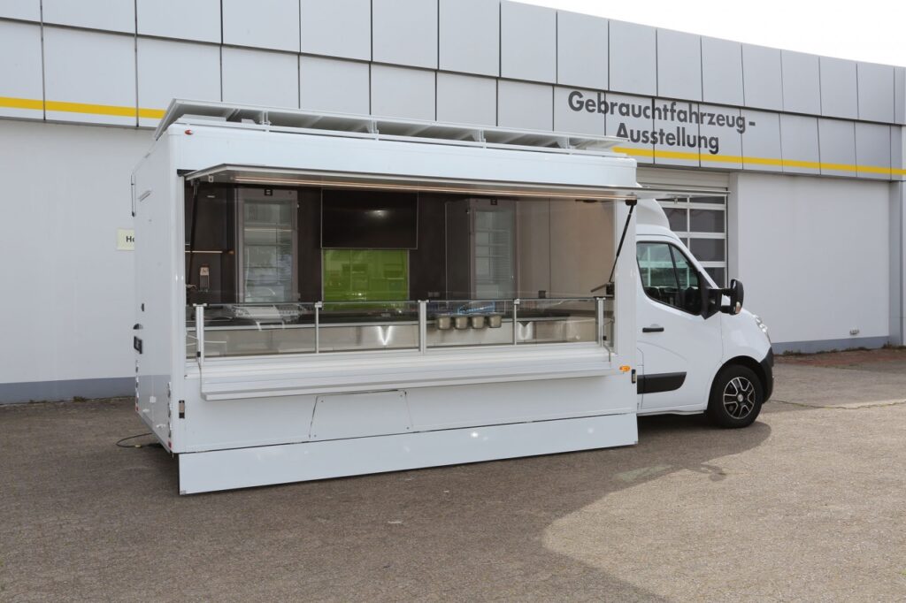 Jahreswagen mit Top Ausstattung: Leichtmetallfelgen schwarz/silberfarbend, elektrisch aufstellbares Dachschild als Werbefront ca. 1300 mm hoch, klappbare Verblendung zum Boden an Verkaufsseite, Radausschnittverkleidung, Flachbildschirm 49 " und Radio mit Lautsprechern im Aufbau, Kühltheke mit 670 mm Auslage, senkrechten Thekenaufsatz und verstärkter Kühlleistung sowie Heißgasabtauautomatik, 2 Kühlschubladen, 2 Hochkühlschränke mit Glastür, 1 Gefrierschrank, LED-Lichtband HO, Werbetafel mit Glasschriftfeld uvm.